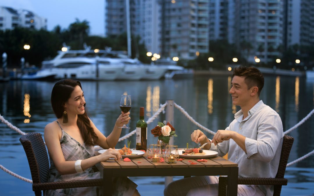 Couple enjoying food and wine on a floating bar in Sentosa Cove, Singapore.