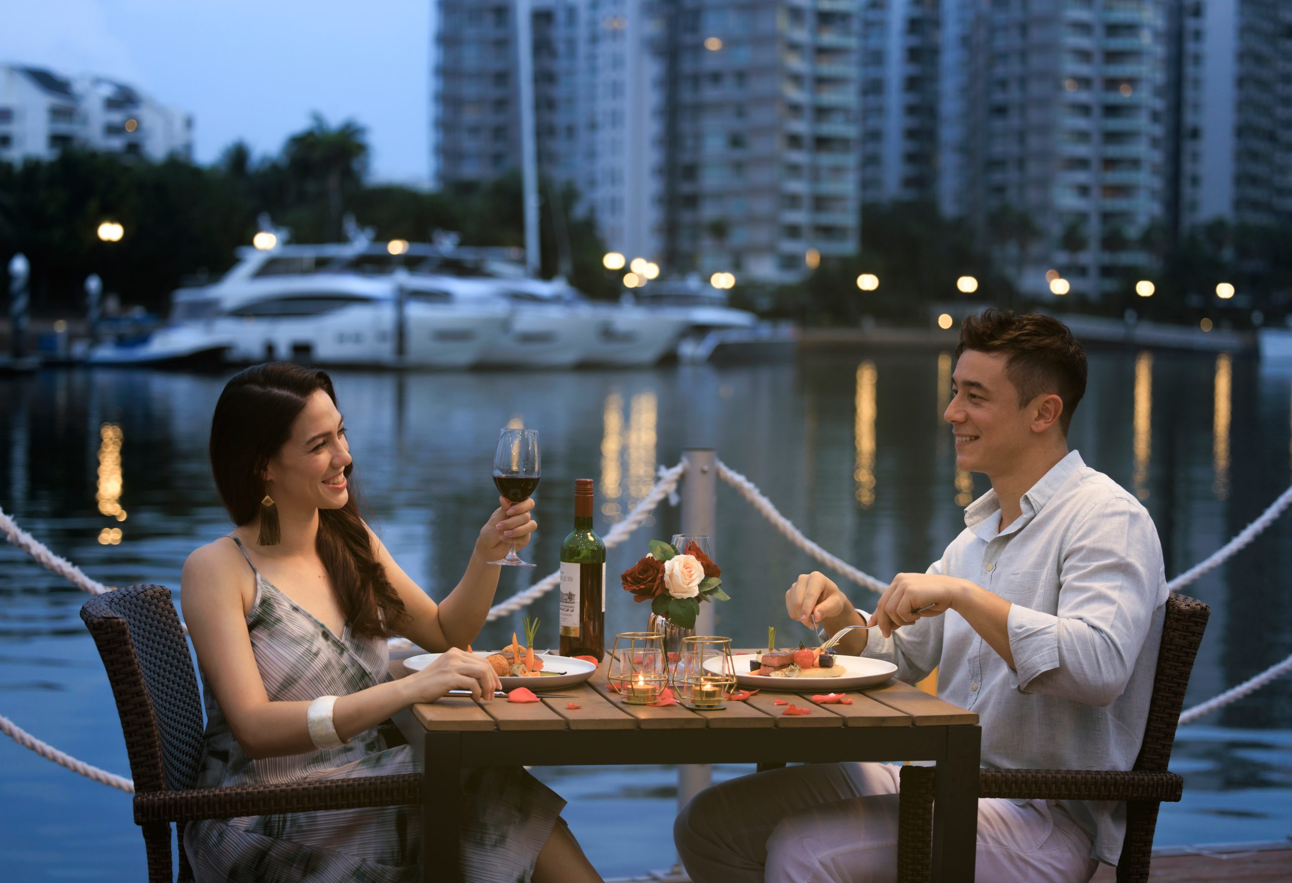 Couple enjoying food and wine on a floating bar in Sentosa Cove, Singapore.
